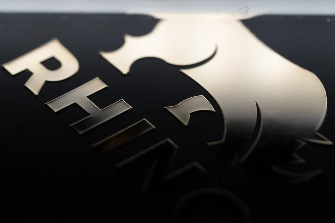 Macro DSLR photograph of an electroformed brushed and polished nickel transfer logo RHINO applied to a matte black surface with no background film